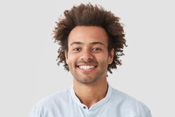 curly-man-with-broad-smile-shows-perfect-teeth-being-amused-by-interesting-talk-has-bushy-curly-dark-hair-stands-indoor-against-white-b.jpg